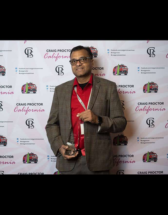 He proudly with an award in front of a step-and-repeat banner for Craig Proctor California, showcasing his achievement.